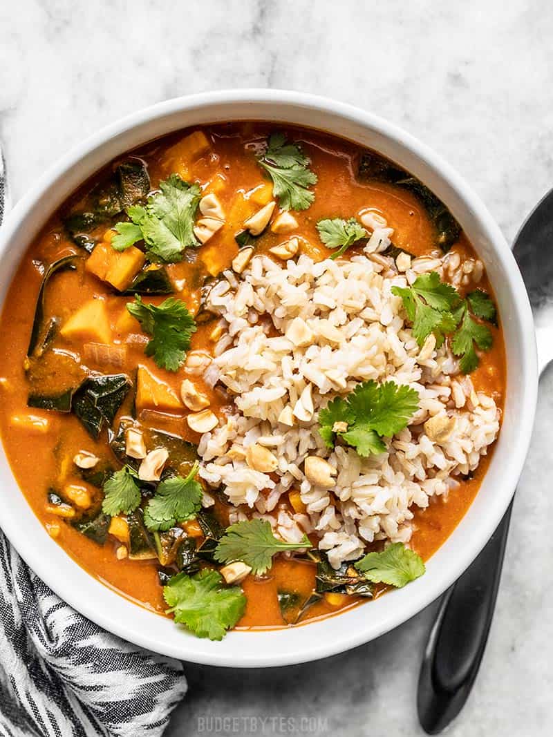 With a rich peanut and tomato sauce, sweet potatoes, collard greens, and crunchy peanuts, this Vegan West African Peanut Stew is comfort in a bowl! Budgetbytes.com A white bowl of Vegan West African Peanut Stew with brown rice and cilantro.