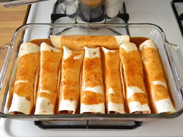 Enchilada sauce poured over rolled enchiladas in baking dish and ready to bake