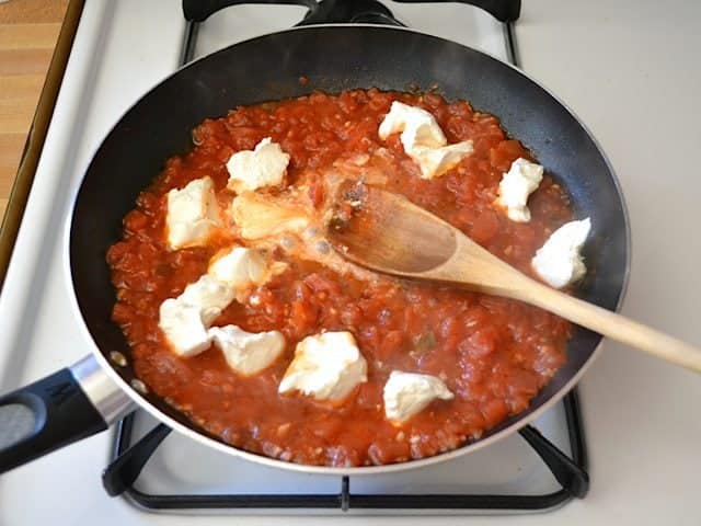Melting cream cheese added to tomatoes in skillet