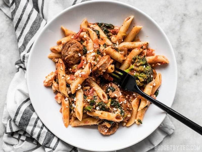 This super easy and satisfying, "sweep the kitchen" Penne Pasta with Sausage and Greens is an entire meal in one pot. Cook once, eat all week. A plate full of Penne Pasta with sausage and greens, a black fork in the center