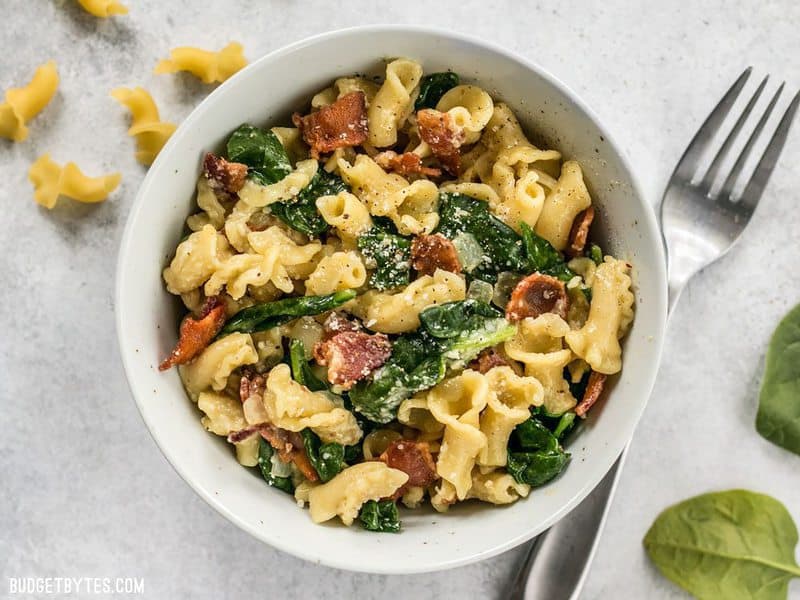 Top view of a bowl of Bacon and Spinach Pasta with Parmesan with a fork on the side