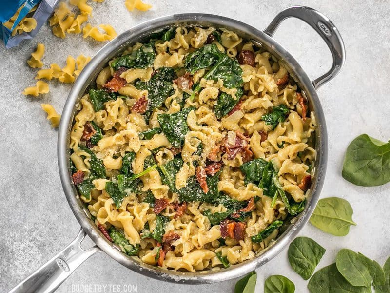 Finished Bacon and Spinach Pasta with Parmesan in a skillet, spinach and dry noodles on the side for staging