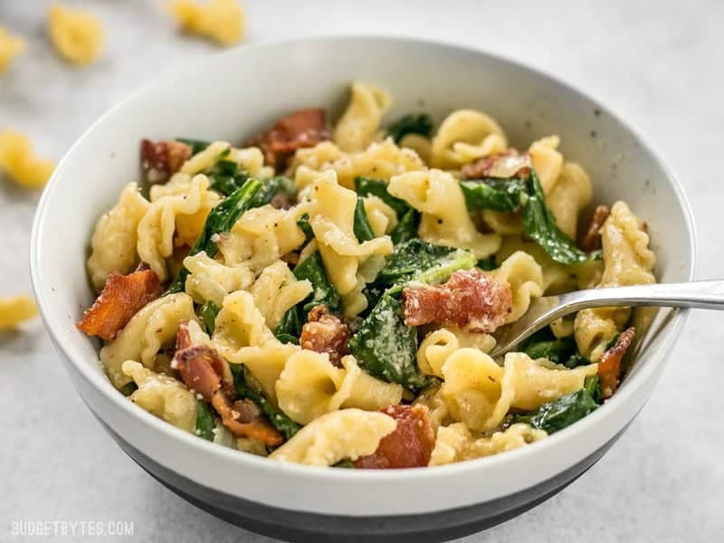 Close up of a bowl of Bacon and Spinach Pasta with Parmesan with a fork