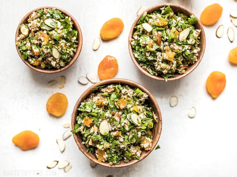 Top view of three bowls of Parsley Salad with Almonds and Apricots, almonds and apricots sprinkled around the bowls for staging