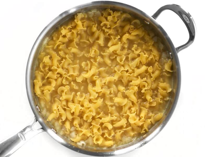Uncooked pasta added to skillet with onions and chicken broth