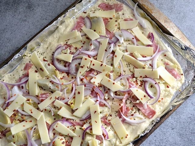 Toppings spread out over flat bread dough on baking sheet