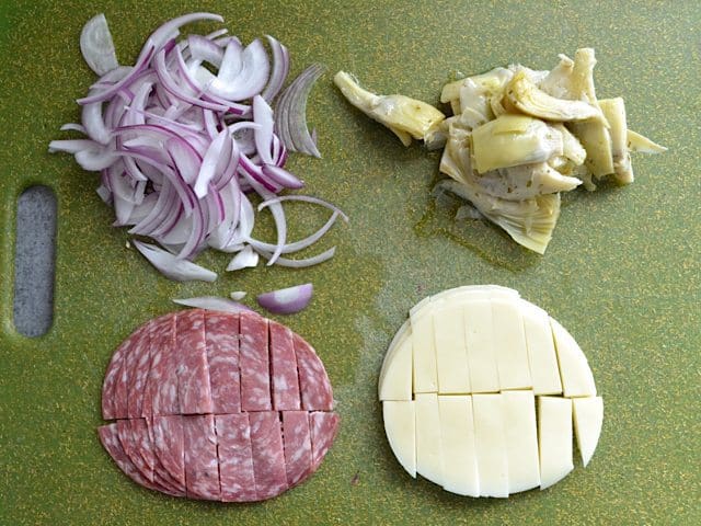Toppings (onions, artichokes, cheese and salami) on cutting board