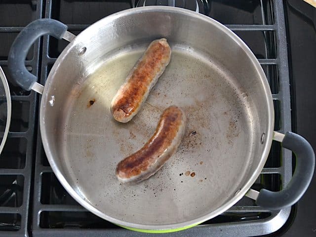 Two sausages in pan browning on stove top