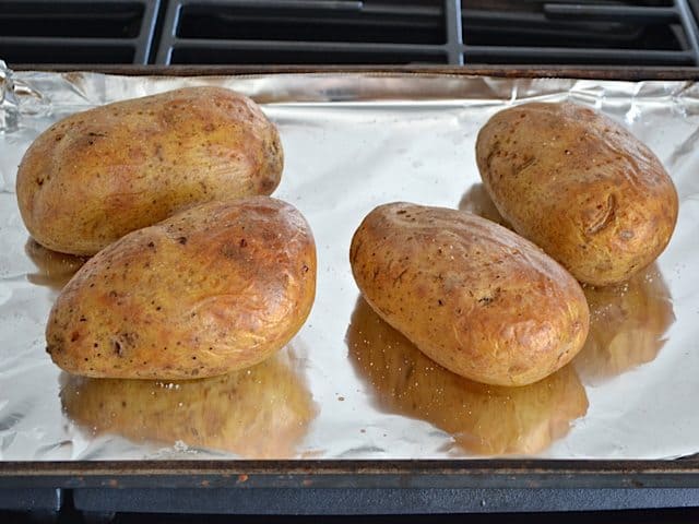 Four potatoes on baking sheet lined with tin foil to bake