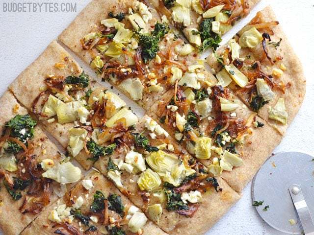 Top view of cooked Caramelized Onion and Artichoke FlatBread cut into slices with pizza cutter