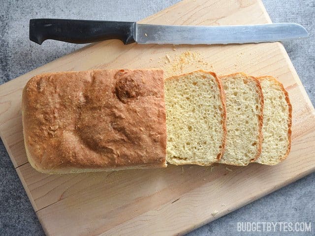 Top view of English Muffin Bread loaf on cutting board with three slices cut off with knife
