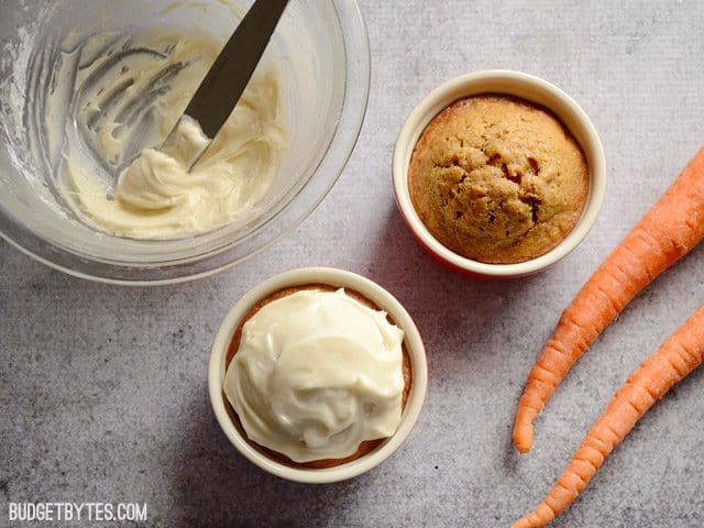 Two carrot cakes with bowl of icing in background, one cake iced