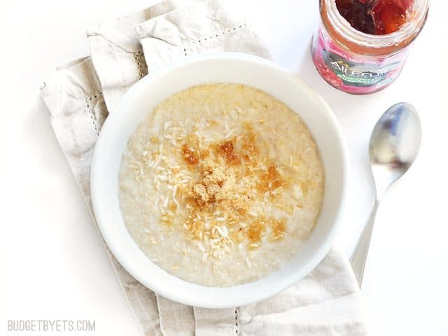 Top view of a bowl of oat brand sitting on a napkin with a spoon and jar of jam on the side