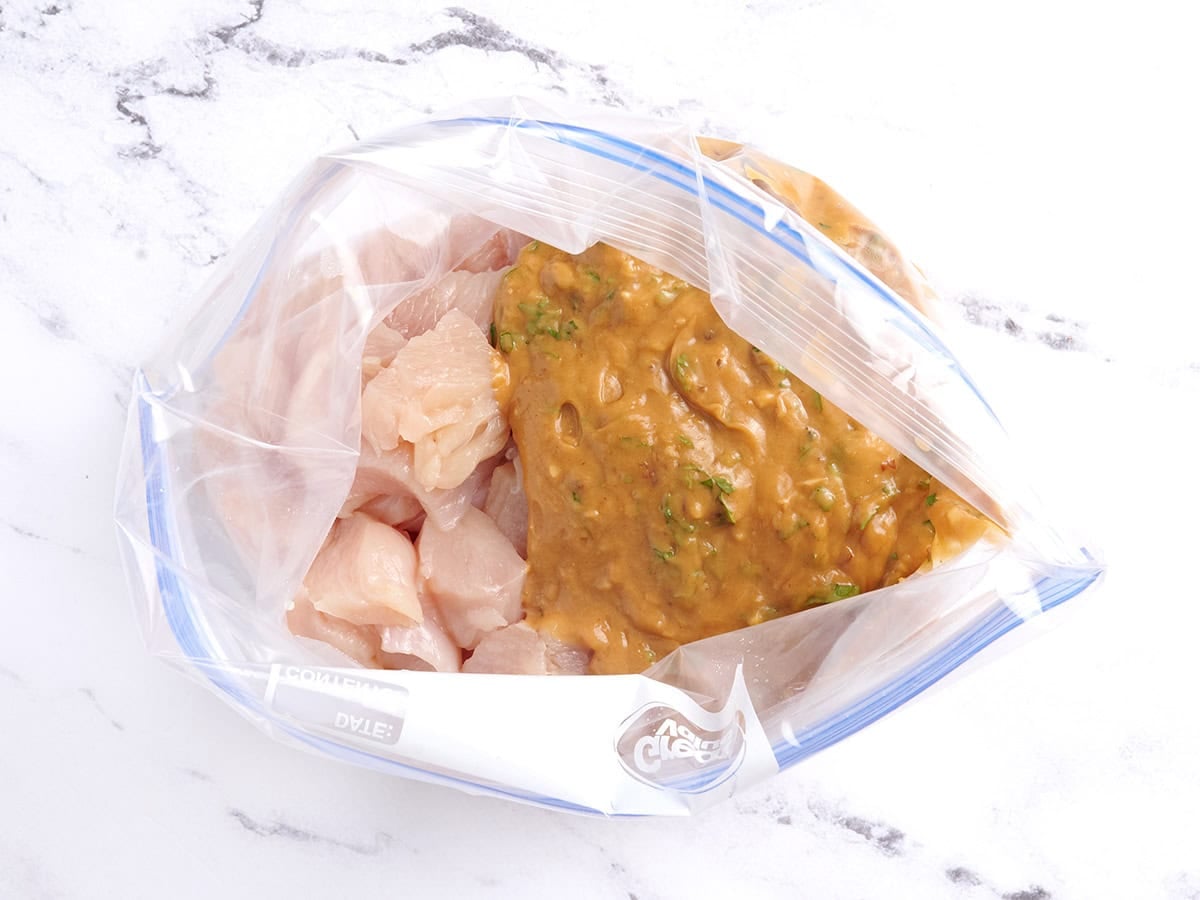 A peanut sauce added to chicken pieces in a bag.