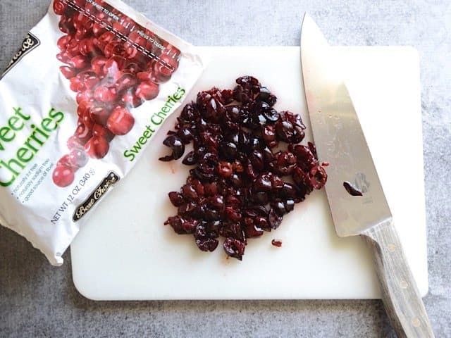 Bag of sweet cherries with some poured onto cutting board and chopped with knife
