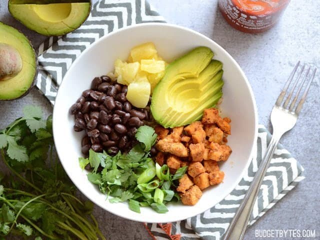 Top view of a Sweet n Spicy Chicken Bowl sitting on a white and gray chevron napkin with a fork on the side