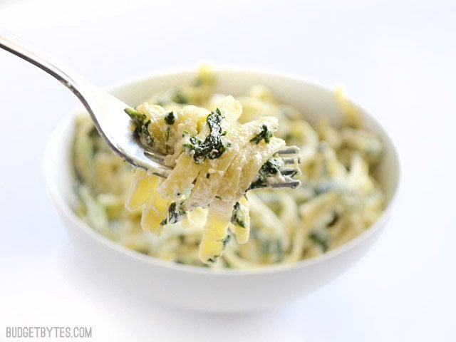 This quick and luxurious Spinach Ricotta Pasta boasts a creamy and garlicky spinach sauce made easy with ricotta cheese. BudgetBytes.com fork Close up view of a forkful of spinach ricotta pasta being lifted from the serving bowl