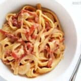 A close-up of pasta with roasted red peppers and herbs with a fork.