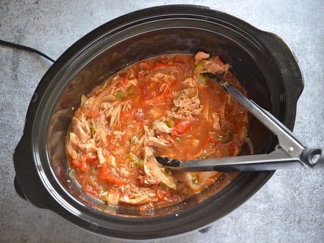 Shredding chicken with tongs in slow cooker