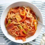 A bowl of three pepper pasta on top of a blue striped tablecloth.