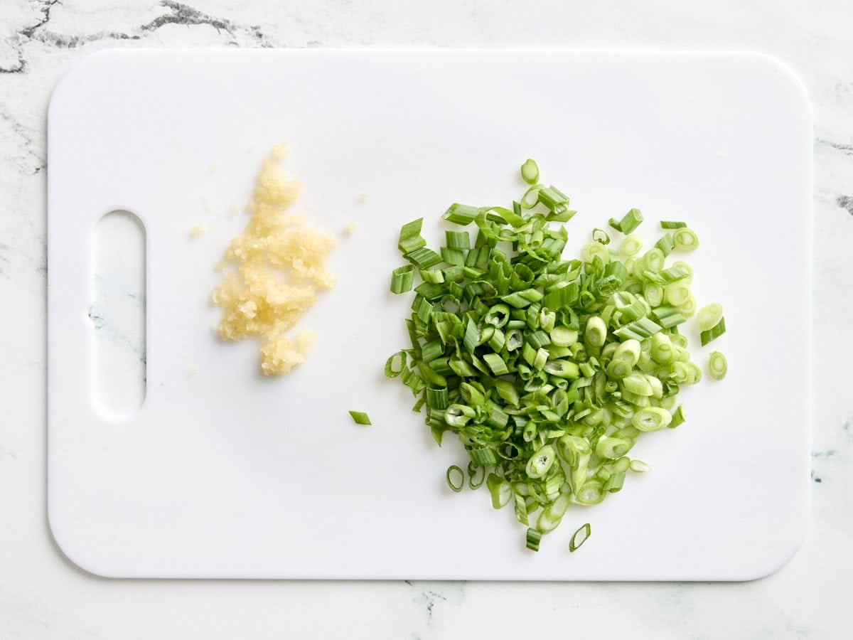 Diced green onions and minced garlic on a cutting board.
