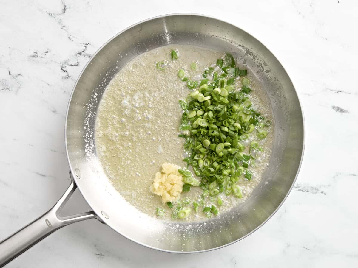 Melted butter in a skillet with sliced green onions and minced garlic.