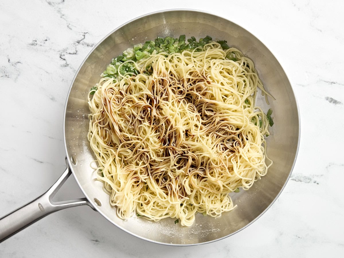 Garlic noodles with sauce added in a skillet.