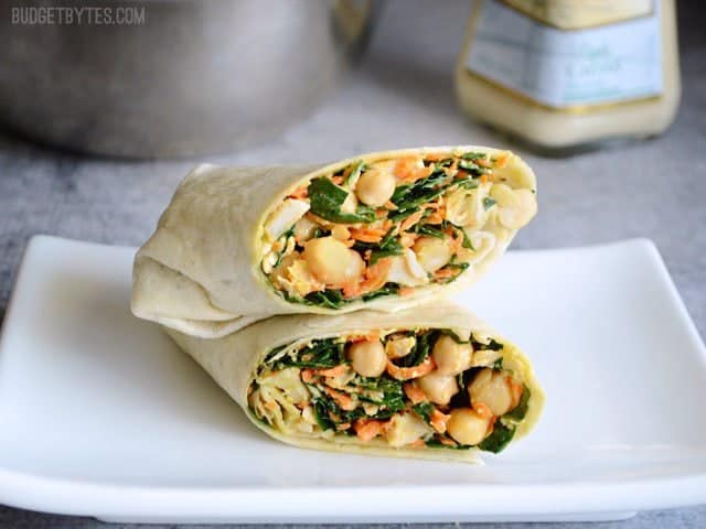 This easy Chicken Kale Caesar Wrap is a great no-cook, no-reheat lunch idea. A big deli-style wrap made at home for a LOT less money. Budetbytes.com A Kale Chicken Caesar Wrap cut in half on a plate