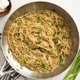 Overhead view of garlic noodles in a skillet, topped with sliced green onions.