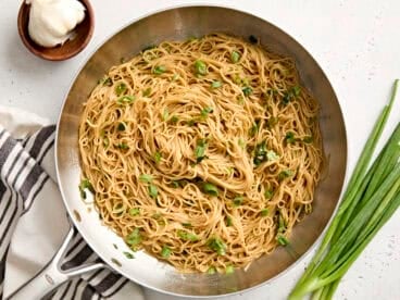 Overhead view of garlic noodles in a skillet, topped with sliced green onions.