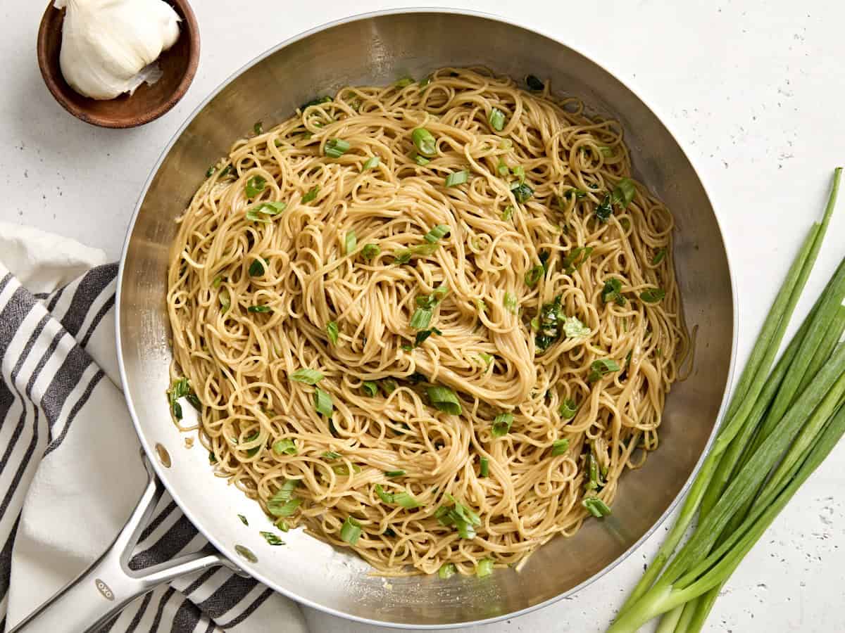 Overhead view of garlic noodles in a skillet, topped with sliced green onions.