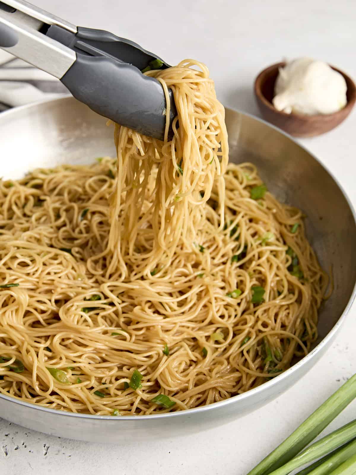 Garlic Noodles are sweet, rich, and savory with a strong garlic punch. They make the perfect side dish to any Asian inspired meal. BudgetBytes.com Side view of garlic noodles in a skillet with kitchen tongs taking some.