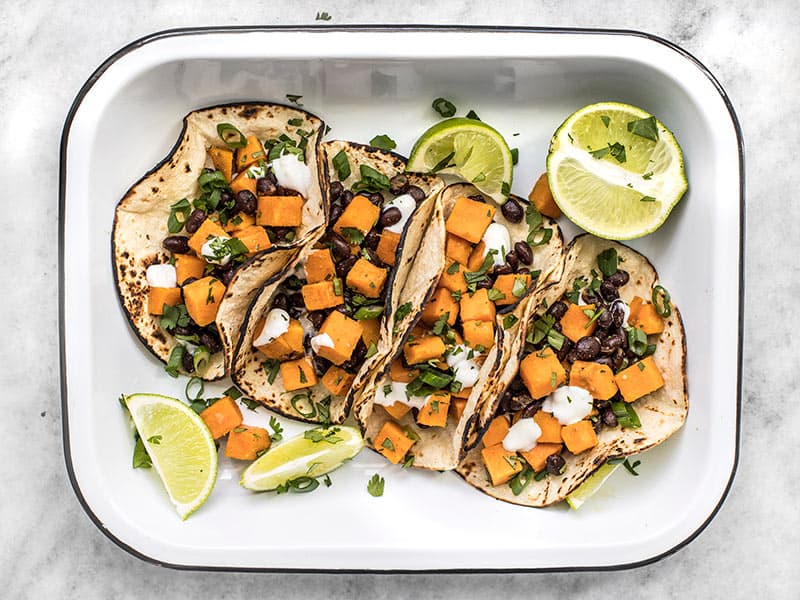 These light and refreshing Sweet Potato Tacos are filled with a simple sweet potato and black bean hash, and topped with a tangy lime crema. Budetbytes.com Overhead view of sweet potato tacos in a serving dish with lime and cilantro