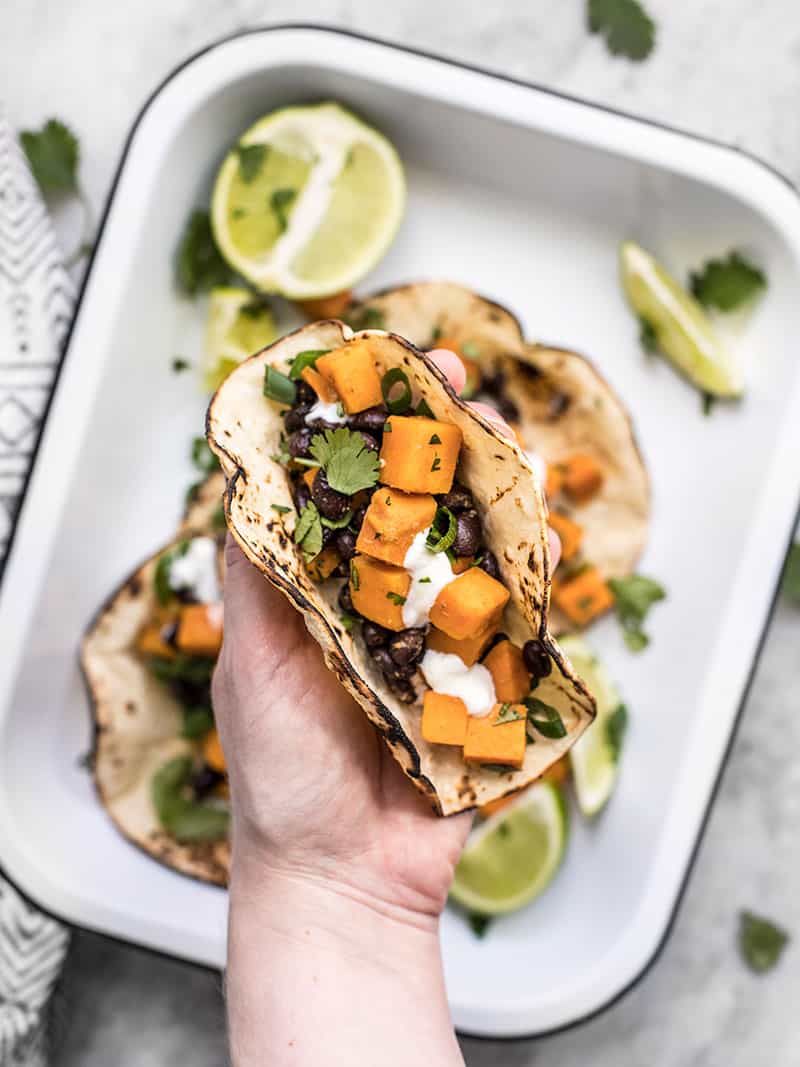 These light and refreshing Sweet Potato Tacos are filled with a simple sweet potato and black bean hash, and topped with a tangy lime crema. Budetbytes.com A hand holding a sweet potato taco close to the camera