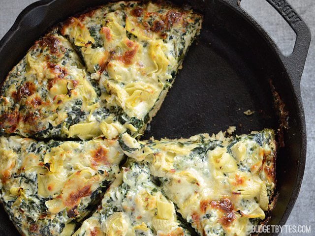 A rich and garlicky spinach cream sauce, artichoke hearts, and melty mozzarella make this thick crust Spinach Artichoke Pizza ultra indulgent! Budetbytes.com Close up of the baked and sliced Creamy Spinach Artichoke Pizza, with one slice missing