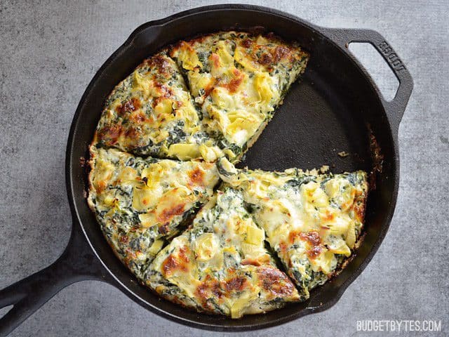 A rich and garlicky spinach cream sauce, artichoke hearts, and melty mozzarella make this thick crust Spinach Artichoke Pizza ultra indulgent! Budetbytes.com Creamy Spinach Artichoke Pizza in a cast iron skillet, one slice removed