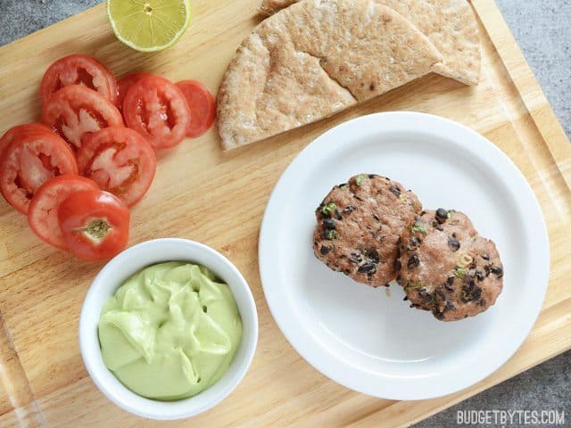 These flavorful mini black bean turkey burgers come together quickly and bake in the oven for a fast, no fuss dinner. Step by step photos. Budetbytes.com Two Mini Black Bean Turkey Burgers on a plate with pita and toppings on the side