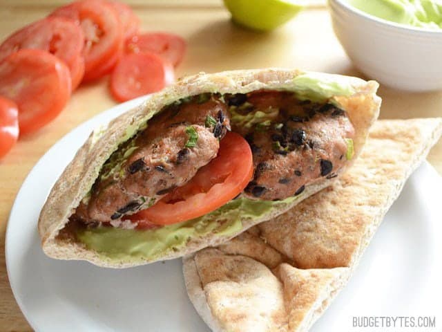 These flavorful mini black bean turkey burgers come together quickly and bake in the oven for a fast, no fuss dinner. Step by step photos. Budetbytes.com Two Cooked Mini Black Bean Turkey Burgers in a pita with avocado and tomato