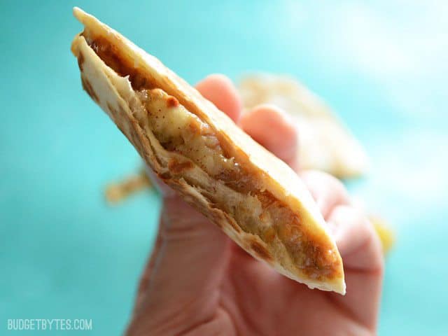 Need a quick dessert? Use your over ripe bananas in this caramelized banana, peanut butter, and cinnamon "quesadilla." The perfect single portion dessert! Budetbytes.com Side view of a cut Caramelized Banana and Peanut Butter Quesadillas being held close to the camera
