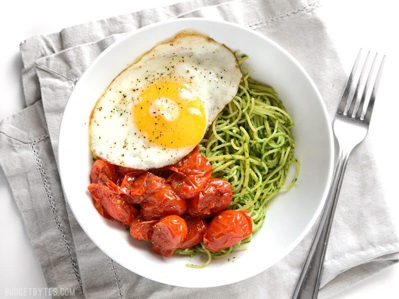 Vibrant green parsley pesto pasta pairs perfectly with sweet blistered cherry tomatoes and a the creamy yolk of a fried egg. Simple, delicious food. Budetbytes.com Overhead view of a bowl full of parsley pesto pasta with blistered tomatoes and a fried egg