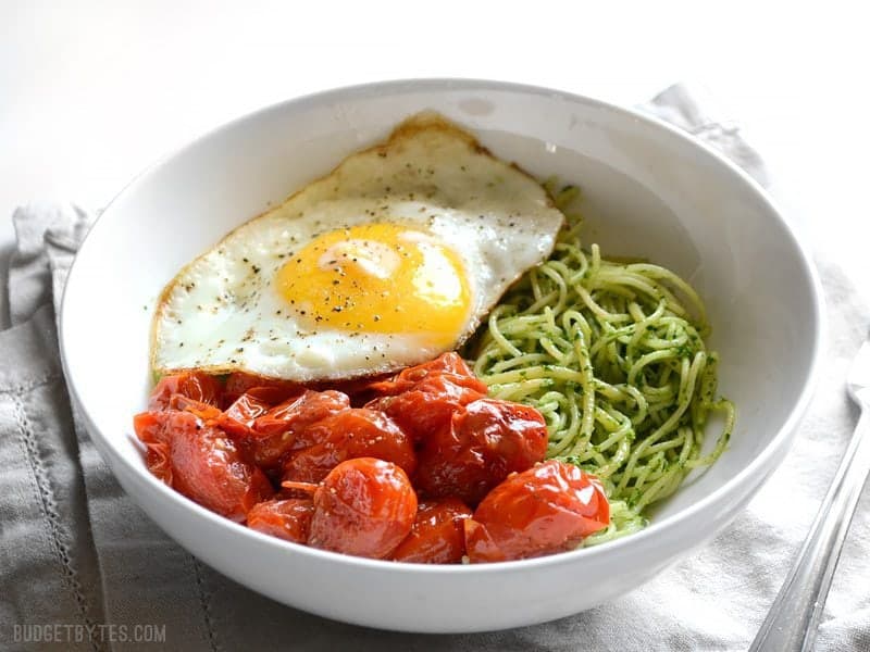 Vibrant green parsley pesto pasta pairs perfectly with sweet blistered cherry tomatoes and a the creamy yolk of a fried egg. Simple, delicious food. Budetbytes.com Side view of the bowl of parsley pesto pasta with tomatoes and fried egg