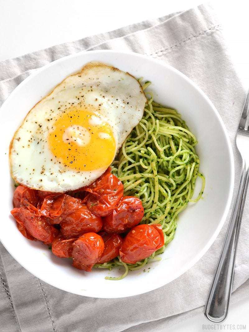 Vibrant green parsley pesto pasta pairs perfectly with sweet blistered cherry tomatoes and a the creamy yolk of a fried egg. Simple, delicious food. Budetbytes.com Overhead view of a bowl full of parsley pesto pasta with blistered tomatoes and a fried egg