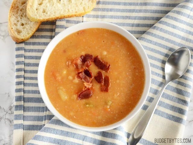 This hearty Bacon Bean and Potato Soup is extra thick with both beans and potato, plus enough bacon and vegetables to give each bowl plenty of flavor! Budetbytes.com Over head view of a bowl of Bacon Bean and Potato Soup ready to serve with bread