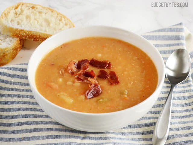 This hearty Bacon Bean and Potato Soup is extra thick with both beans and potato, plus enough bacon and vegetables to give each bowl plenty of flavor! Budetbytes.com Side view of a bowl of Bacon Bean and Potato Soup, topped with bacon
