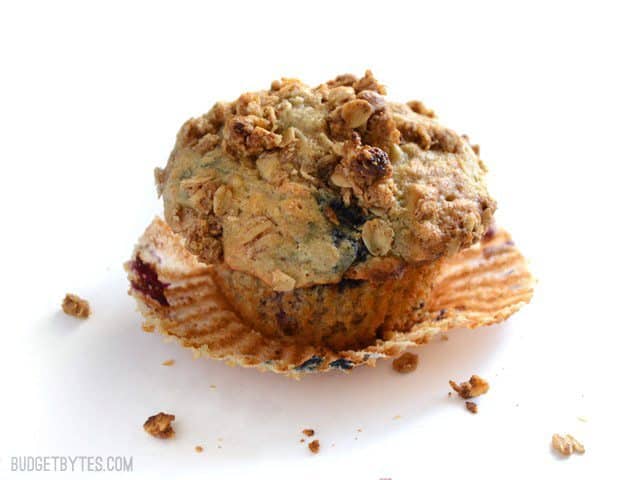 These big, moist, and fluffy Triple Berry Oatmeal Muffins are a real treat for breakfast and boast the goodness of rolled oats. Freezer friendly! Budetbytes.com One Triple Berry Oatmeal Muffin on a white surface with the paper peeled back