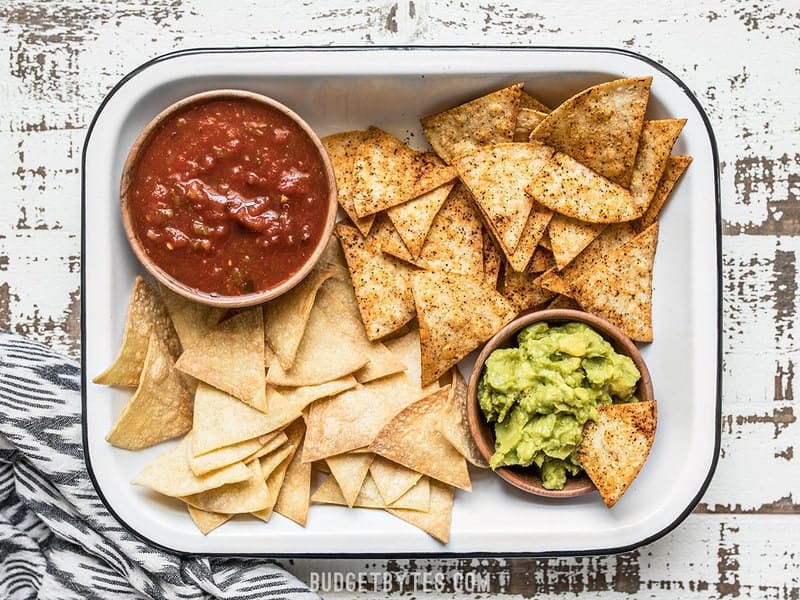 These Homemade Baked Tortilla Chips are fast, easy, super crunchy, a great way to use up leftover tortillas, and a great alternative to store bought chips. Budgetbytes.com A baking dish full of Homemade Baked Tortilla Chips with bowls of salsa and guacamole