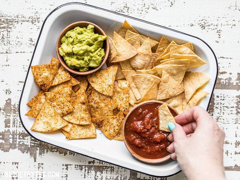 These Homemade Baked Tortilla Chips are fast, easy, super crunchy, a great way to use up leftover tortillas, and a great alternative to store bought chips. Budgetbytes.com A hand dipping a Homemade Baked Tortilla Chip into a bowl of salsa