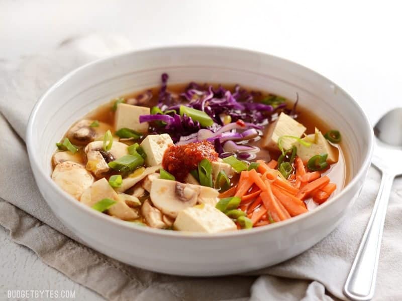 This easy hot and sour soup is light on the stomach, but big on flavor! The spicy and tangy broth is full of colorful vegetables and tender cubes of tofu. BudgetBytes.com Front view of a shallow bowl of vegetables and tofu with hot and sour soup broth