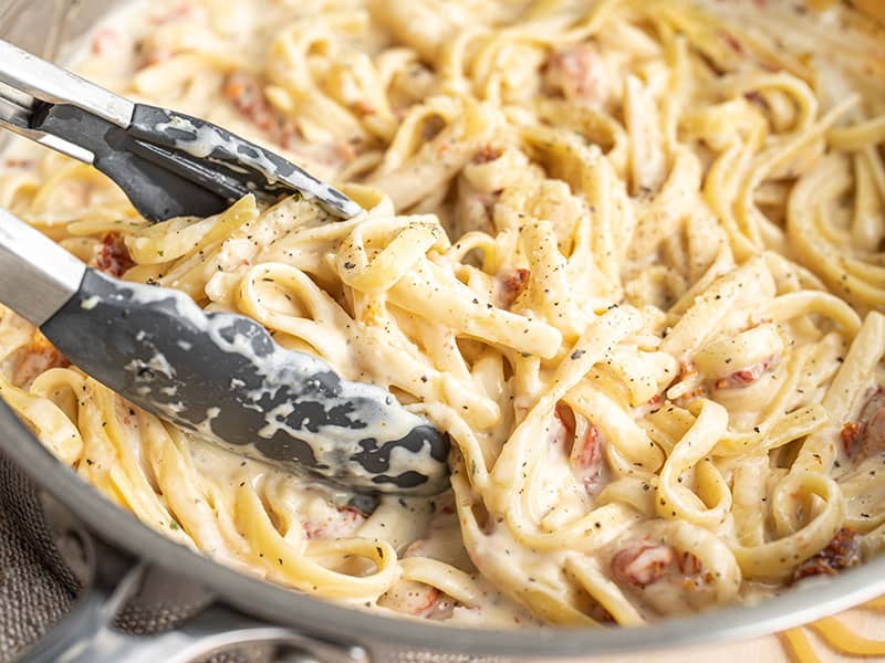 This incredibly fast and easy Creamy Sun Dried Tomato Pasta cooks in 30 minutes and uses just one pot. The perfect quick and satisfying weeknight dinner! Budetbytes.com Close up of tongs picking up a clump of creamy pasta from the skillet