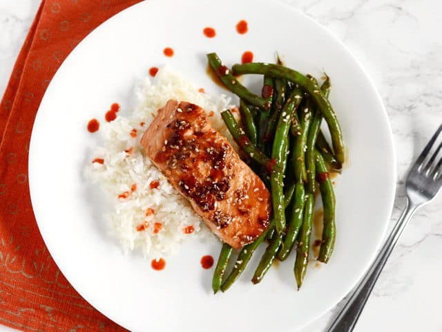 This incredible fast and easy Sesame Glazed Salmon dinner is faster than take-out and fancy enough to impress your friends and family. Budetbytes.com Sesame Glazed Salmon and Green Beans plated with jasmine rice and a drizzle of sriracha